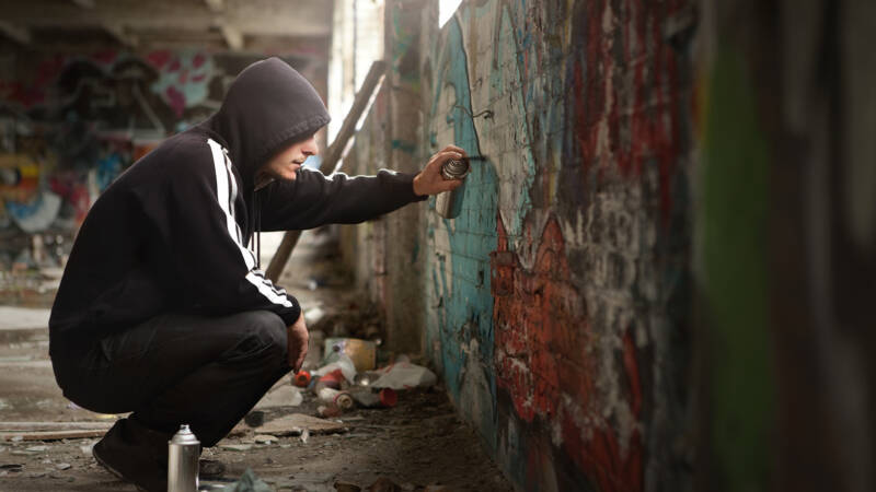 young man in hoodie spraying graffitti